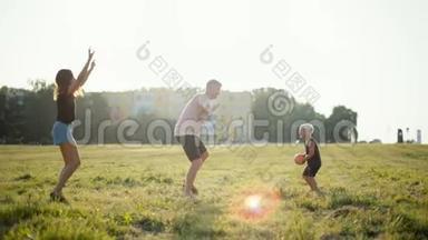 幸福的年轻家庭正在和小孩子在美丽的日落草地上打球